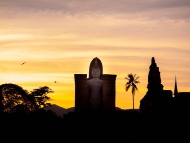 Sukhothai Tarih Parkı 'ndaki Wat Mahathat Tapınağı' nın siluetinin inanılmaz manzarası. Altından günbatımı arka planında büyük bir Buda heykeli Tayland 'daki UNESCO Dünya Mirası Alanı..
