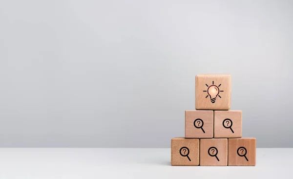 Creative idea and problem solving concept. Light bulb icon sign on top of problem symbol, searching and question mark on wooden cube block stack pyramid shape on white background with copy space.