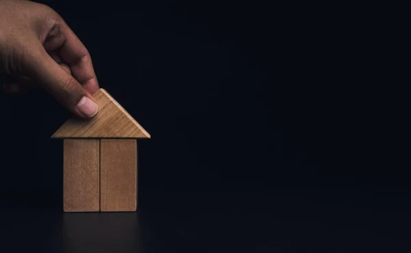 Hand building house with wooden blocks, laying of the roof on dark background with copy space. Property planning. House building construction symbol, eco style, loan concepts.