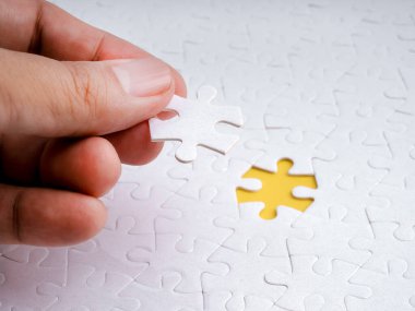 Beyaz yapbozun son parçasına yakın plan yerleştirme, son adımı sembolize etme, çözüm bulma, problem çözme ve iş ve kişisel hedeflerde başarı..