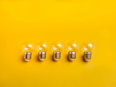 Five clear light bulbs lined up on yellow background. Concept of creative ideas, innovation, brainstorming, teamwork, leadership, and bright thinking in business or education context.