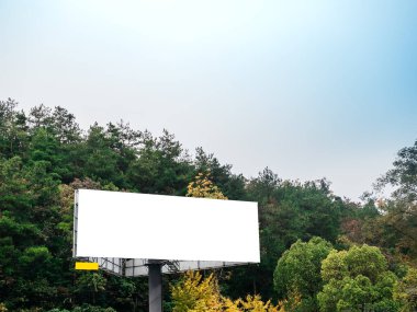 Açık gökyüzünün altında, dağ yeşili bir ormanın yanında duran boş beyaz reklam panoları, promosyon kampanyaları ve doğal ortamlarda tasarım sunumları için ideal..