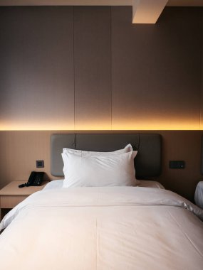 Modern otel odası, temiz beyaz yatak odası, hafif ışıklandırma, ve minimalist dekor, huzurlu ve rahat bir atmosfer yaratıyor rahatlama, seyahat konaklama ve konukseverlik hizmetleri için mükemmel.