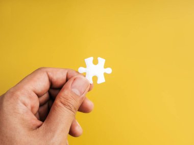 Sarı arka planda tek bir beyaz yapboz parçası, karmaşık sistemlerde kritik kayıp, temel element, son adım, problem çözme, takım çalışması ve anahtar bileşeni sembolize eder..