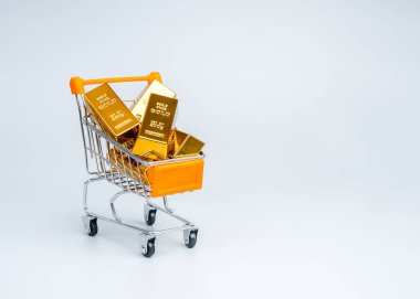 Beyaz arka plandaki bir alışveriş arabasındaki altın külçeleri modern ekonomik bağlamda altın yatırımı, zenginlik birikimi, değerli metal ticareti ve finansal büyümeyi temsil etmektedir..