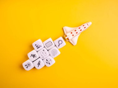 Minimum düzeyde oyuncak roket uzay aracı ve iş simgesi blokları, sarı arka plan. Başlangıç, dijital pazarlama stratejisi, yenilik ve büyüme başarısı konsepti için modern iş planlaması.