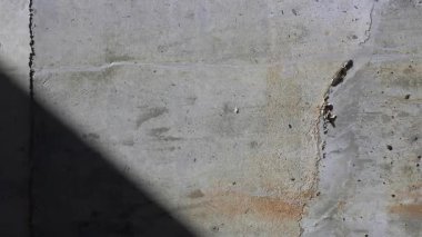 Sert beton yüzeyi, çatlakları ve güçlü güneş ışığı ve gölgesi altında yıpranmış lekeleri olan çiğ beton duvar dokusu. Endüstriyel mimari arkaplan ve grunge doku fon kavramı.