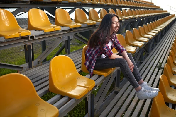 Beautiful lonely woman sitting on tribunes and laughs — Stock Photo, Image