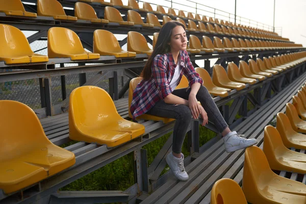 Beautiful lonely woman sitting on tribunes and looks aside. — Stock Photo, Image