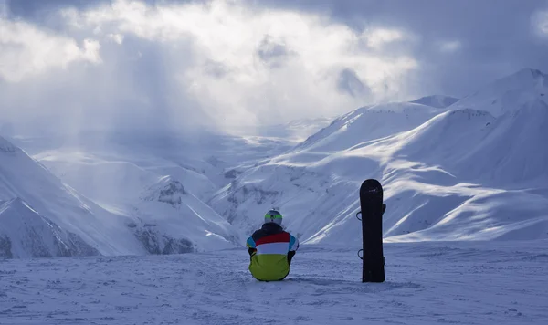 Snowboarder zitten en kijken naar de berg. — Stockfoto