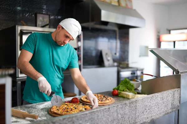Szef kuchni cięcia świeżo przygotowaną pizzę na podłoże drewniane. — Zdjęcie stockowe