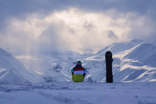 Snowboarder sentado e olhando para a paisagem da montanha de inverno — Fotografia de Stock