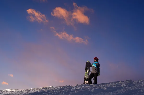 Karanlık gökyüzü günbatımı karşı bir yamaca kızla snowboard standları — Stok fotoğraf