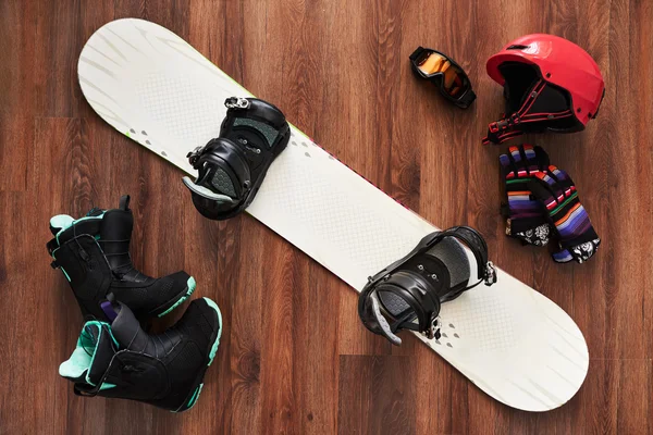 set of snowboard boots, helmet, gloves and mask on wooden