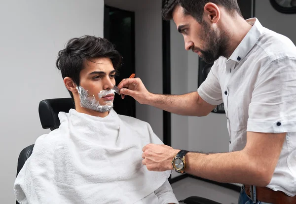 Парикмахер бреет бороду бритвой и пены для бритья — стоковое фото