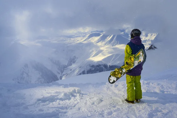Snowboardåkare står och tittar på bergen i snöiga väder — Stockfoto