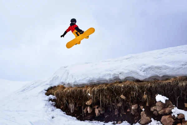 Snowboarder springen van de plank op een besneeuwde heuvel met gras. — Stockfoto