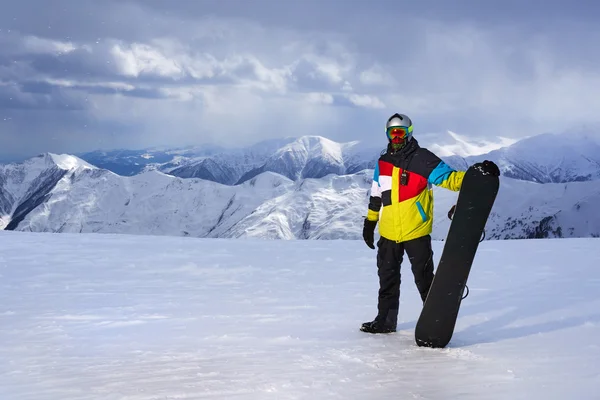 Snowboarder segurando snowboard na mão no fundo das montanhas — Fotografia de Stock