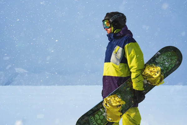 Snowboarder hält ein Brett in der Hand. Abendlicher Schneefall in den Bergen. — Stockfoto