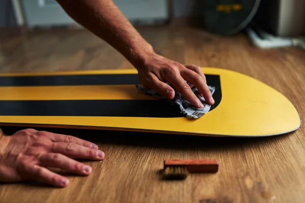Uomo strofina la cera spugna snowboard sul pavimento di legno — Foto Stock