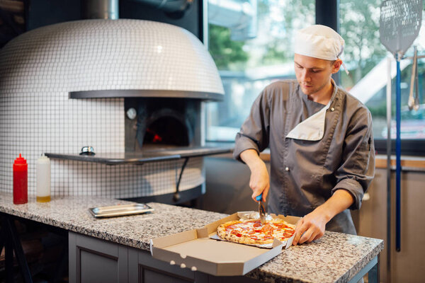 Chef slices pizza in a box. Catering kitchen work.