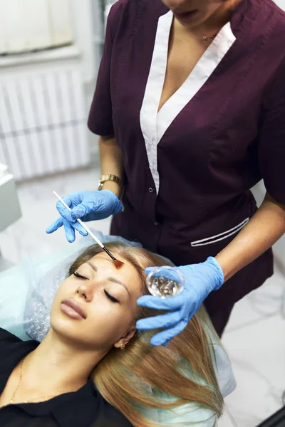 Beautician applicerar fuktgivande kosmetisk gel på flickornas ansikte med en borste. Kosmetisk föryngring. — Stockfoto