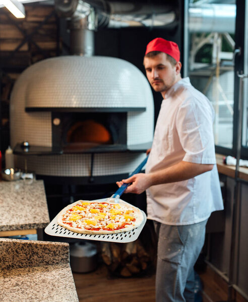 The chef holds the pizza on the special large spatula. Catering kitchen work.