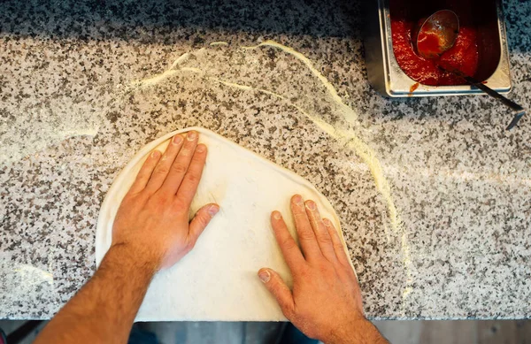 Cook stretches pizza dough with his hands. Catering kitchen work. — Stock Photo, Image