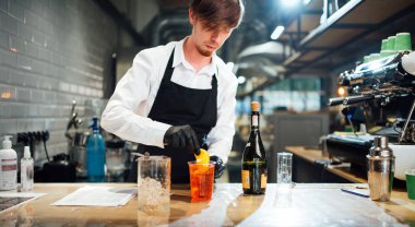 Barmen bardağa bir dilim portakal ve kokteyl koyar. İçme hazırlama süreci.