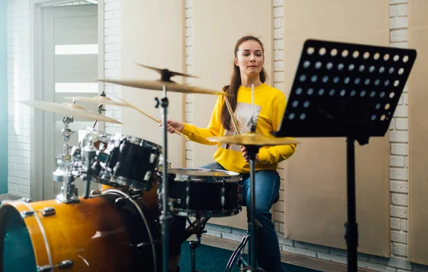 Ung kvinna tittar på noter medan hon spelar trummor. Lektion på musikskolan. — Stockfoto