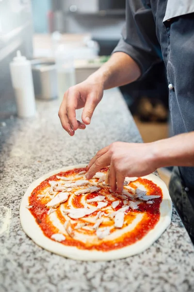 O cozinheiro derrama os ingredientes para a pizza na massa com molho. Construção de cozinha para refeições. — Fotografia de Stock