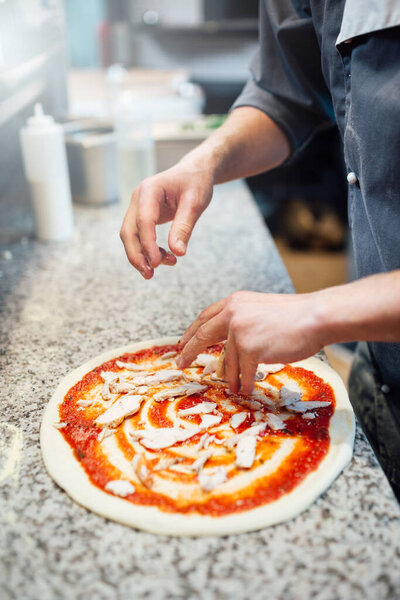 Chef pours the ingredients for the pizza on the dough with sauce. Catering kitchen work.
