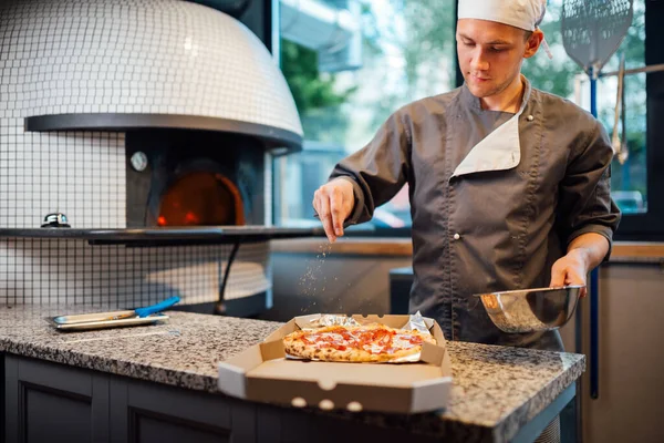 Lo chef spruzza la pizza in una scatola con spezie. Lavori di ristorazione cucina. — Foto Stock