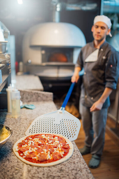 Cook takes pizza on the spatula. Catering kitchen work.