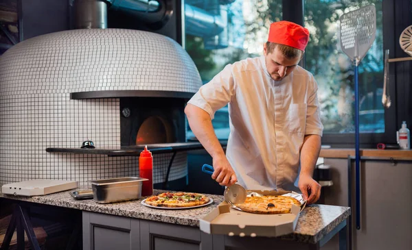 De chef snijdt de pizza in de doos. Keukenwerk voor catering. — Stockfoto