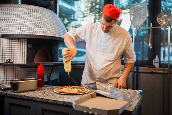 The chef pours sauce on pizza. Catering kitchen work.