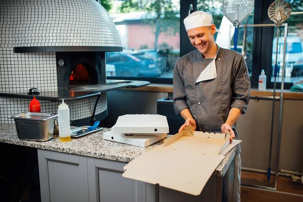 Joyful pizzeria werker maakt een pizzadoos. Keukenwerk voor catering. — Stockfoto