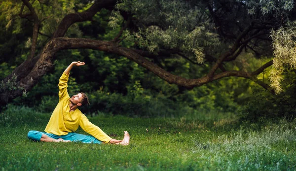 Man doing parivrtta janu sirsasana right exercise. Qigong practice in the park. — Stock Photo, Image