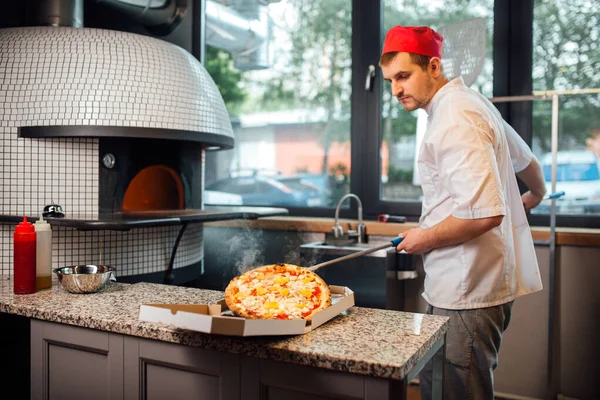 Il cuoco mette la pizza sulla spatola in una scatola. Lavori di ristorazione cucina. — Foto Stock