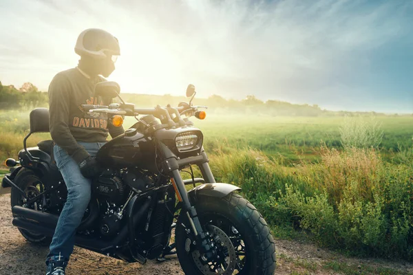 Motociclista ao amanhecer senta Harley Davidson Fat Bob 114 2020 em uma motocicleta no campo. — Fotografia de Stock