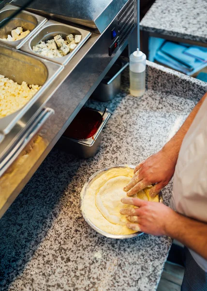 Lo chef dispone la pasta della pizza in una teglia da forno. Lavori di ristorazione cucina. — Foto Stock