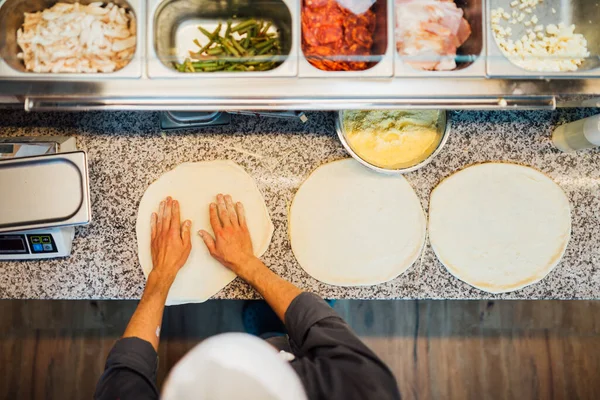 Szef kuchni ugniata ciasto pizzowe rękami z góry widok. Kuchnia cateringowa. — Zdjęcie stockowe