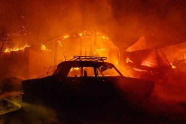 Arka planında yanan bir ev olan yanmış bir araba.