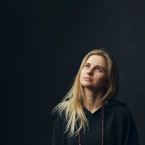 Mujer rubia yogi de pie en sudadera con capucha negra sobre fondo oscuro. — Foto de Stock