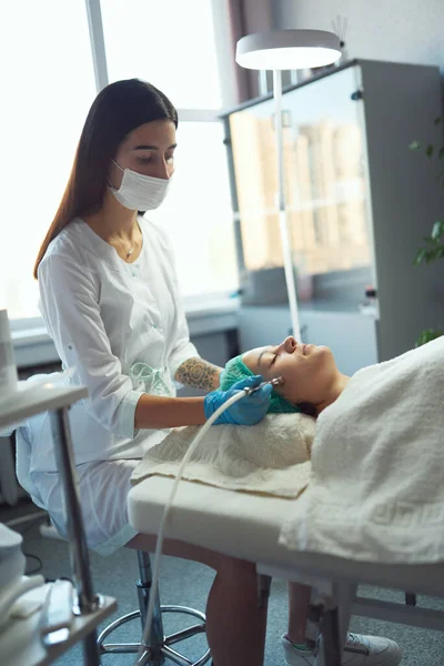 Косметолог делает процедуру микродермабразия кожи лица молодой женщины в салоне красоты. — стоковое фото
