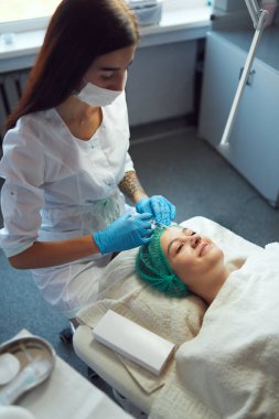 Güzellik uzmanı genç bir kızın yüzüne dolgu maddesi enjekte ediyor..