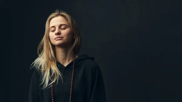 Mujer rubia con capucha negra meditar sobre fondo oscuro. — Foto de Stock