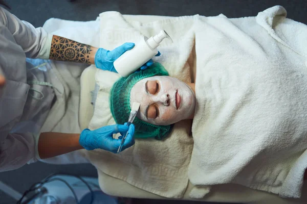 Güzellik uzmanı genç bir kadının yüzüne yüz maskesi takıyor. Cilt bakımı ve kozmetik prosedürü. — Stok fotoğraf