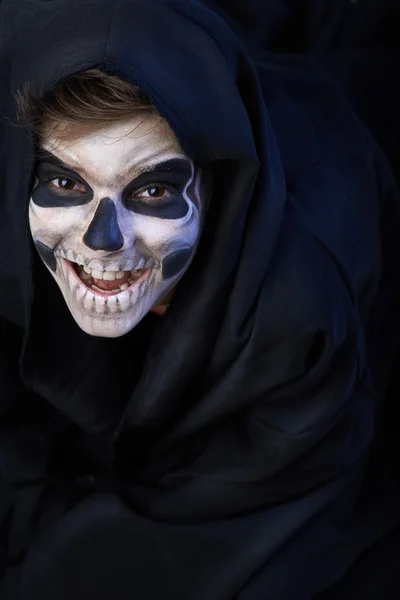 Teen with make-up of skull in black cloak laughs — Stock Photo, Image