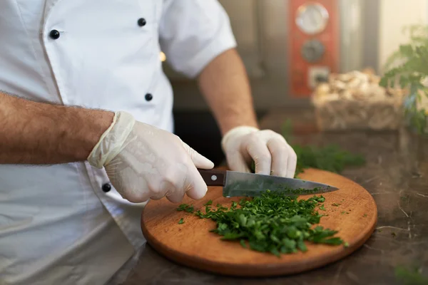 Koch hackt frische Kräuter auf Holzbrett — Stockfoto